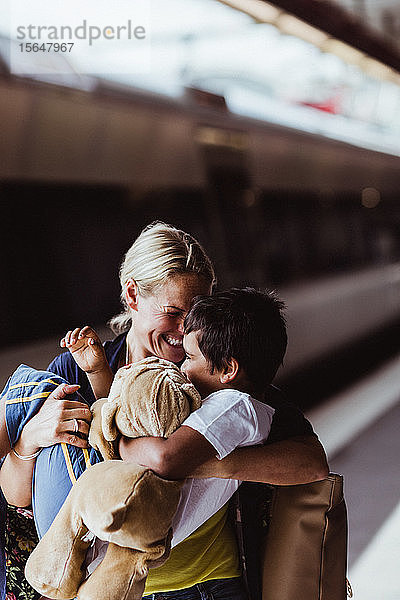 Glückliche Mutter  die einen Sohn trägt  während sie am Bahnhof steht