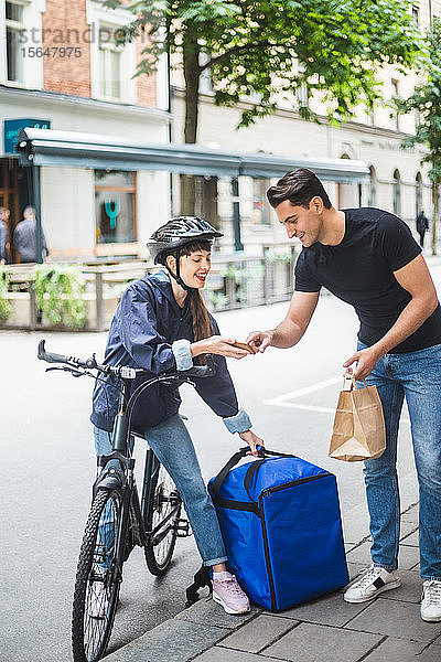 Zustellerin nimmt Zeichen eines männlichen Kunden entgegen  während sie ein Paket auf der Straße in der Stadt ausliefert