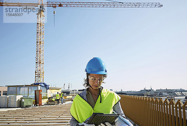 Selbstbewusste Architektin in reflektierender Kleidung mit digitalem Tablet auf der Baustelle gegen klaren Himmel