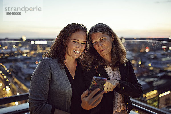 Geschäftsfrauen  die nach der Arbeit auf der Terrasse stehen und sich am Smartphone selbstständig machen