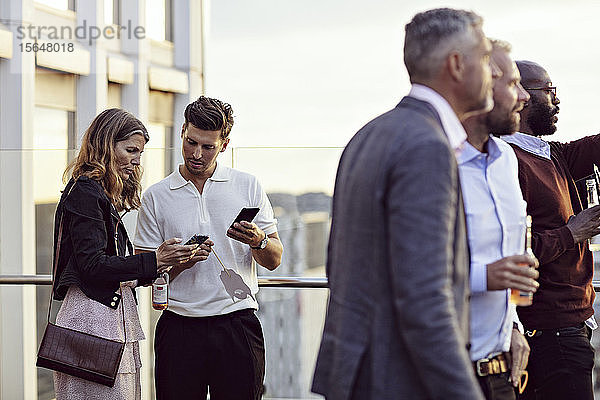 Berufstätige  die sich über Smartphones unterhalten  während ihre Kollegen nach der Arbeit im Büro feiern