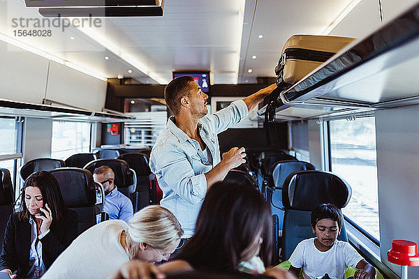 Mann richtet Koffer im Regal aus  während er mit der Familie im Zug während der Ferien reist