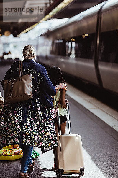 Rückansicht von Mutter und Tochter zu Fuß mit Gepäck auf dem Bahnsteig des Bahnhofs