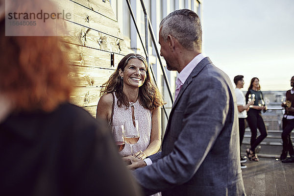 Lächelnde Geschäftsfrau im Gespräch mit Kollegen bei einer Party auf der Terrasse