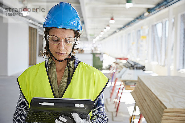 Selbstbewusste Architektin in reflektierender Kleidung mit digitalem Tablett auf der Baustelle