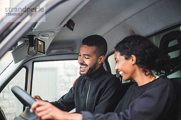 Lächelnder männlicher Spediteur  der seinem Kollegen ein Mobiltelefon zeigt  während er im Lastwagen sitzt