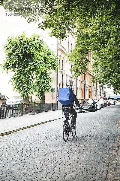 Rückansicht eines Lebensmittellieferanten  der auf der Straße in der Stadt Fahrrad fährt