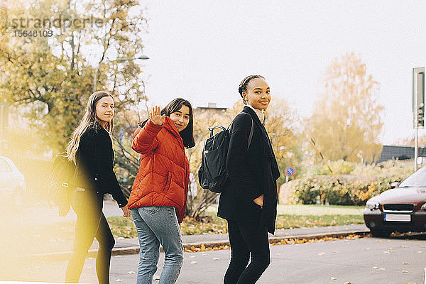 Porträt von lächelnden Teenager-Freunden  die zusammen auf der Straße in der Stadt spazieren gehen