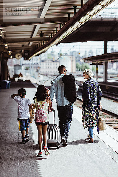 Mann mit Gepäck spricht am Bahnhof zu Fuß mit seiner Familie