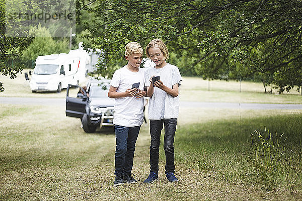 Ein Mädchen zeigt seinem Bruder ein Handy  während sie auf dem Campingplatz steht