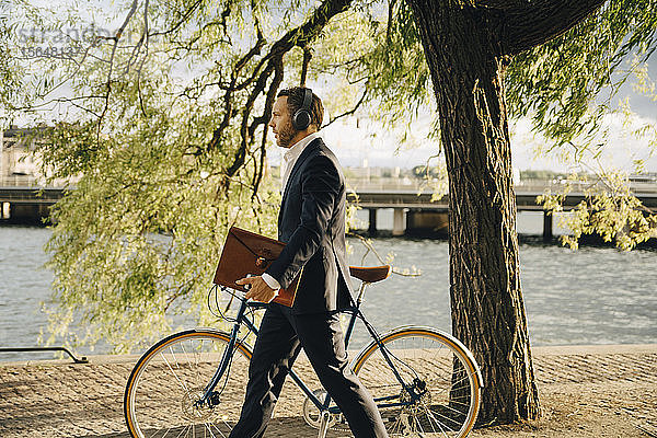 Seitenansicht eines Geschäftsmannes  der mit dem Fahrrad auf einem Fußweg unterwegs ist  während er über Kopfhörer Musik hört