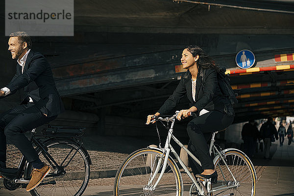 Lächelnder Geschäftsmann und Geschäftsfrau fahren Fahrrad auf der Straße in der Stadt