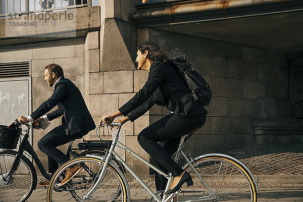 Seitenansicht eines Geschäftsmannes und einer Geschäftsfrau  die auf der Straße in der Stadt Fahrrad fahren