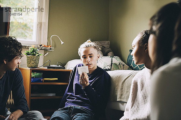 Freunde schauen Teenager an  der beim Spielen im Schlafzimmer Plakate liest