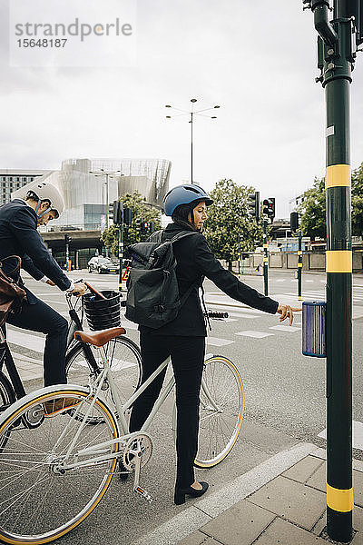Geschäftsfrau mit Fahrrad  die ein Fußgängersignal auf der Straße in der Stadt benutzt