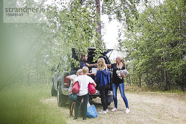 Eltern mit Kindern  die im Urlaub auf dem Campingplatz Gepäck aus dem Auto ausladen