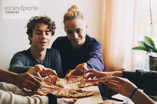 Männliche und weibliche Freunde im Teenageralter nehmen zu Hause Pizzastücke vom Tablett