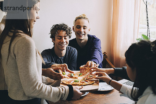 Teenager-Mädchen serviert glücklichen Freunden am Esstisch Pizza