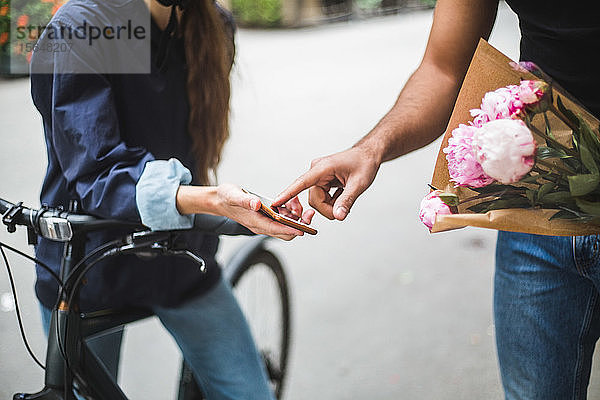 Mitten in der Zustellungsfrau  die ein Zeichen von einem männlichen Kunden entgegennimmt  während sie einen Blumenstrauß auf der Straße in der Stadt überbringt
