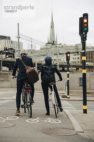 Rückansicht eines Geschäftsmannes und einer Geschäftsfrau mit Fahrrädern auf der Stadtstraße