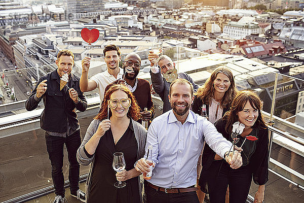 Portrait eines fröhlichen Geschäftsteams mit Requisiten und Getränken bei der After-Work-Party auf der Terrasse