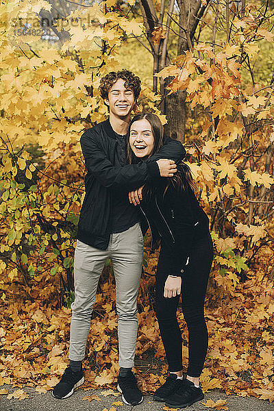 Glückliche Teenager-Freunde lächeln im Herbst in voller Länge gegen die Bäume