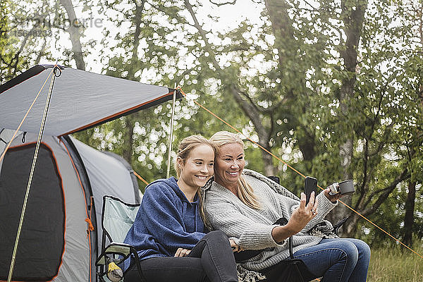 Glückliche Mutter nimmt während des Zeltcampings mit ihrer Tochter Selfie am Smartphone