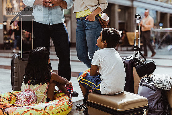 Kinder  die den Eltern zuhören  während sie mit Gepäck am Bahnhof warten