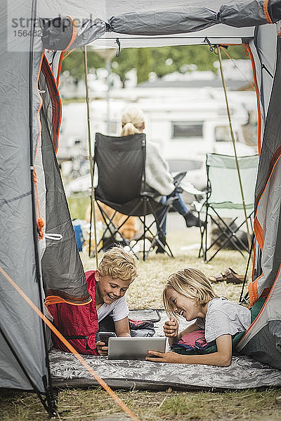 Glückliche Geschwister mit digitalem Tablet für Geschwister im Zelt auf dem Campingplatz