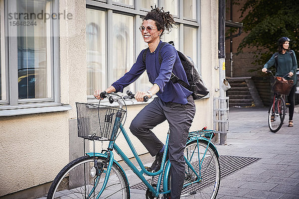 Lächelnde junge Architektin fährt Fahrrad auf der Straße in der Stadt