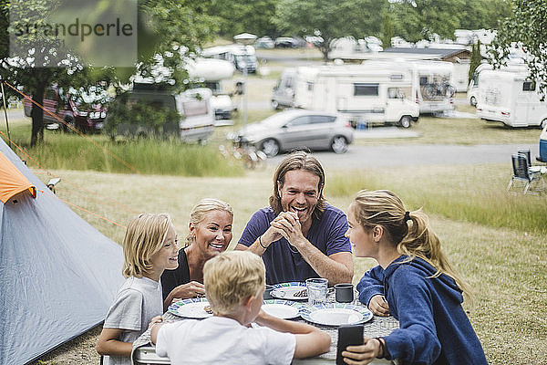 Glückliche Familie unterhält sich beim gemeinsamen Essen am Tisch im Zelt