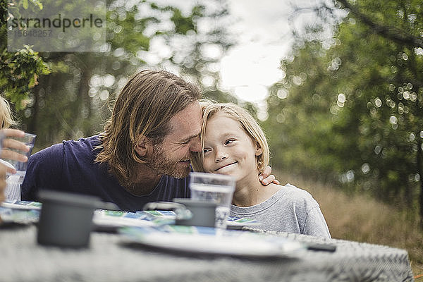 Zärtlicher Vater umarmt Tochter bei Tisch auf dem Campingplatz