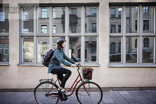 Seitenansicht einer Ingenieurin beim Fahrradfahren auf der Straße beim Gebäude in der Stadt