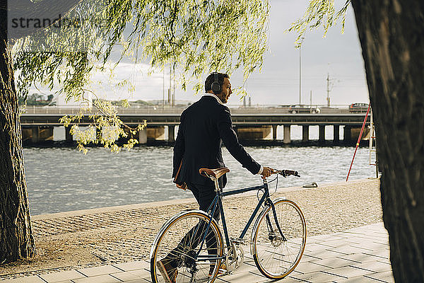 Geschäftsmann zu Fuß mit dem Fahrrad auf dem Fußweg am Kanal in der Stadt