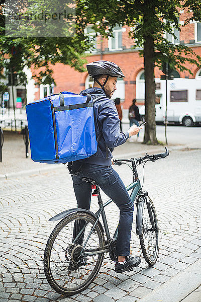 Lebensmittellieferant mit Fahrrad mit Smartphone auf der Straße in der Stadt