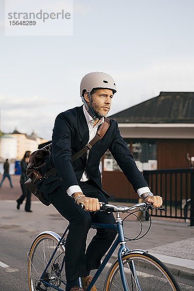 Selbstbewusster Geschäftsmann fährt Fahrrad auf der Straße in der Stadt