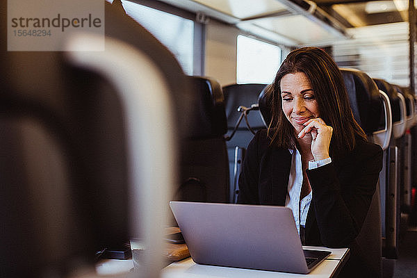 Lächelnde Geschäftsfrau benutzt Laptop  während sie im Zug sitzt