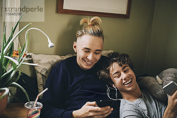 Glückliche Teenager-Jungen  die Musik hören  während sie zu Hause Mobiltelefone benutzen