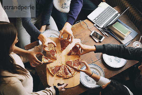 Schrägaufnahme von Freunden  die am Esstisch Pizzastücke nehmen