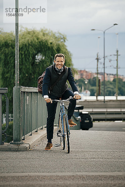 Porträt eines lächelnden Geschäftsmannes beim Fahrradfahren auf einer Brücke in der Stadt