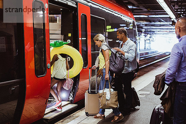 Familie mit Gepäck steigt gemeinsam am Bahnsteig des Bahnhofs in den Zug