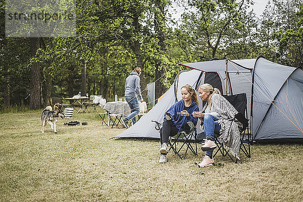 Mutter und Tochter beim Kaffee trinken  während sie auf dem Campingplatz ein Handy anschauen