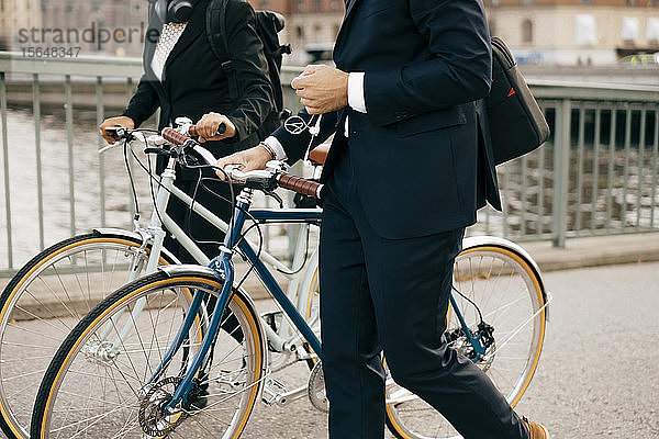 Mittendrin Geschäftsmann und Geschäftsfrau zu Fuß mit Fahrrädern auf einer Brücke in der Stadt