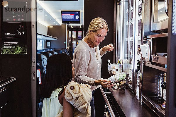 Mutter steht mit ihrer Tochter im Zugkühlschrank und sieht sich Lebensmittel an