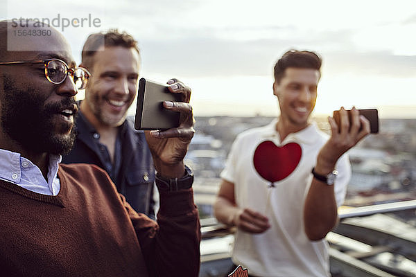 Männliche Berufstätige beim Fotografieren mit Smartphones auf Büroparty