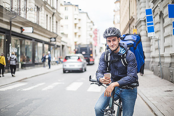 Porträt eines selbstbewussten Lebensmittellieferanten mit Fahrrad auf der Straße in der Stadt