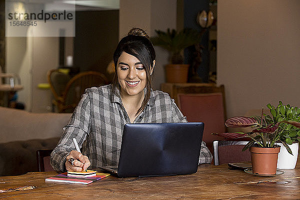 Frau schreibt Notizen und arbeitet am Laptop im Arbeitsraum