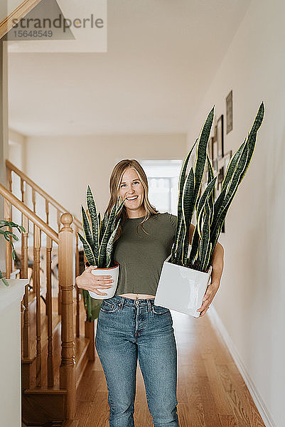 Frau trägt große und kleine Töpfe mit Zimmerpflanzen