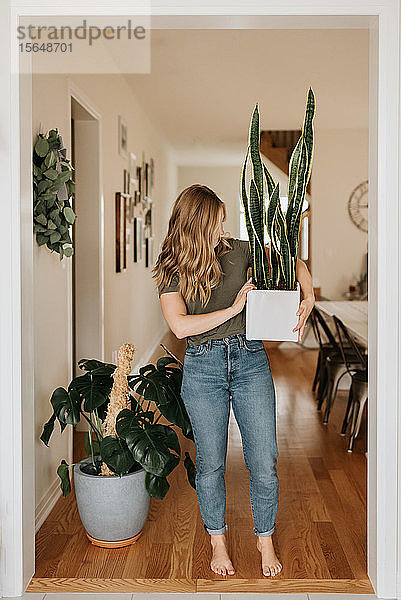 Frau trägt großen Topf mit Zimmerpflanze