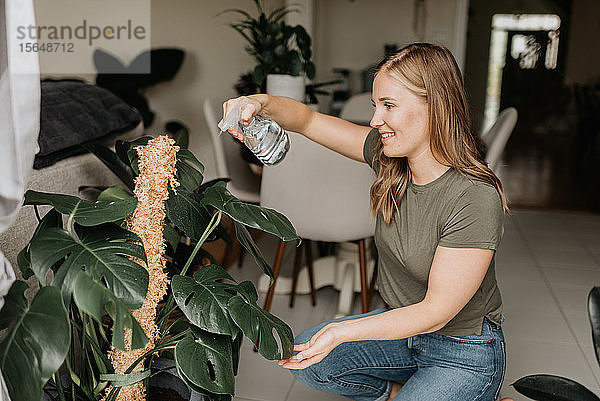 Frau besprüht Zimmerpflanzen mit Wasser
